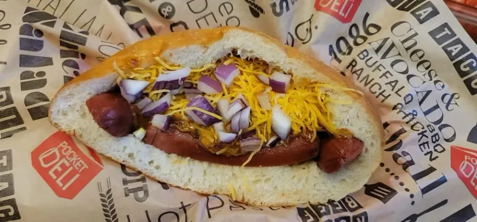 Hot dog with sliced onions and shredded cheddar cheese on a bun.